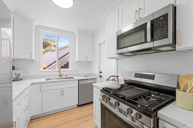 kitchen featuring appliances with stainless steel finishes, light countertops, a sink, and light wood finished floors