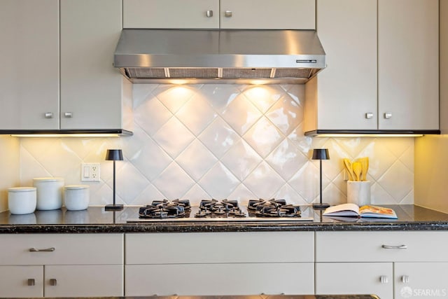 kitchen featuring tasteful backsplash, dark stone countertops, range hood, white cabinetry, and gas cooktop