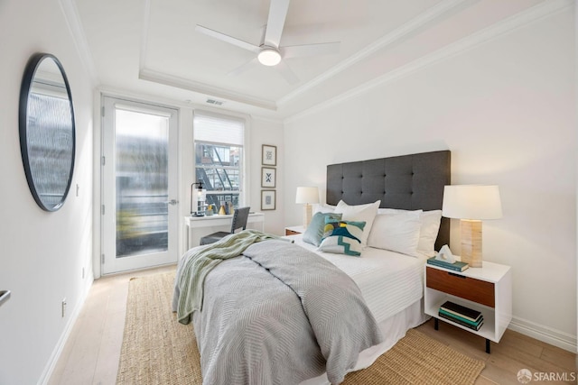 bedroom featuring light wood finished floors, access to outside, a tray ceiling, and crown molding