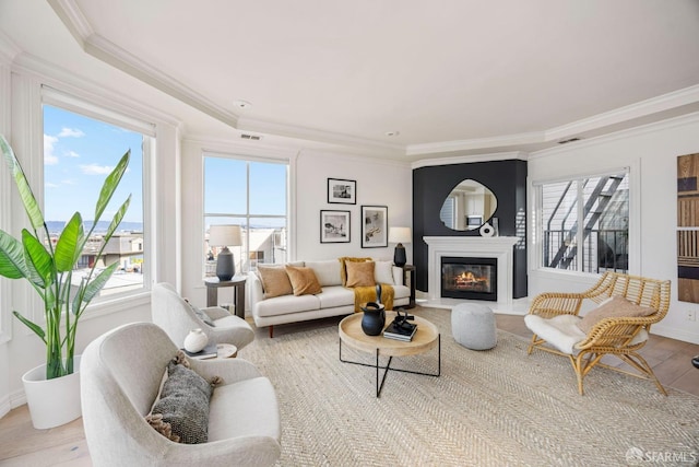 living area with visible vents, ornamental molding, a wealth of natural light, and a glass covered fireplace