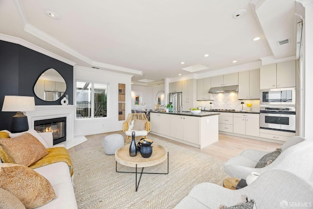 living area featuring crown molding, recessed lighting, visible vents, a glass covered fireplace, and light wood-type flooring