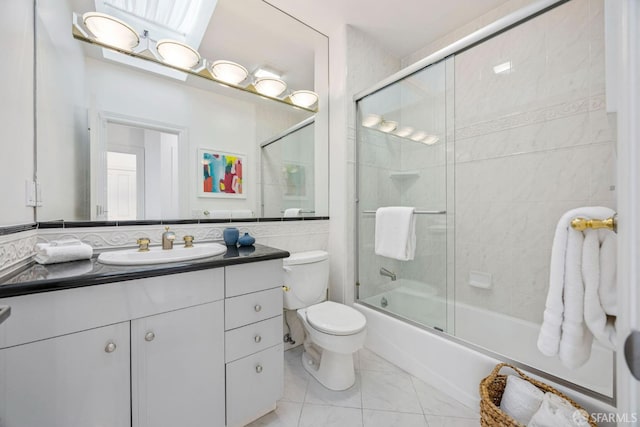 bathroom with toilet, bath / shower combo with glass door, vanity, and tile walls