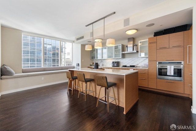 kitchen featuring a kitchen island, glass insert cabinets, a breakfast bar, oven, and wall chimney range hood