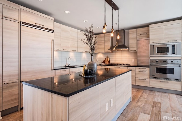 kitchen featuring appliances with stainless steel finishes, light hardwood / wood-style floors, wall chimney exhaust hood, a kitchen island, and sink