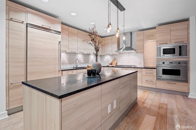 kitchen with stainless steel appliances, light wood-type flooring, a center island, sink, and wall chimney range hood