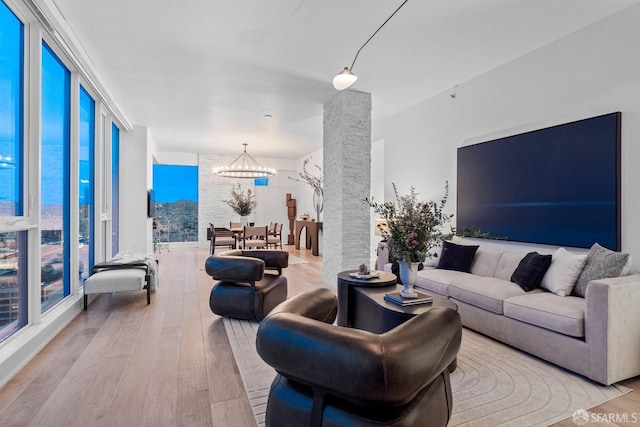 living room with an inviting chandelier, a wealth of natural light, a water view, and light wood-type flooring