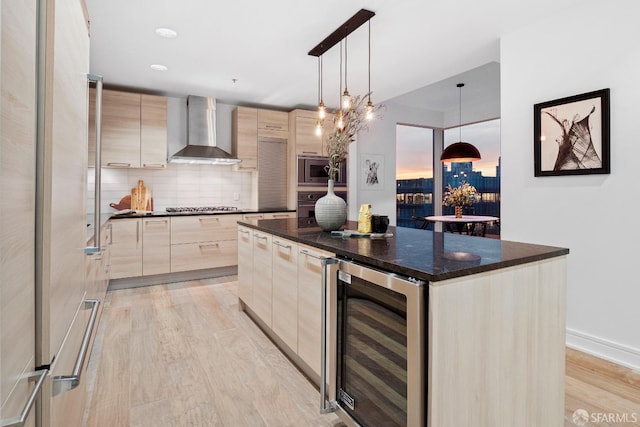 kitchen featuring beverage cooler, decorative light fixtures, wall chimney exhaust hood, a center island, and light wood-type flooring