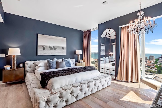 bedroom featuring multiple windows, a water view, light hardwood / wood-style flooring, and a notable chandelier