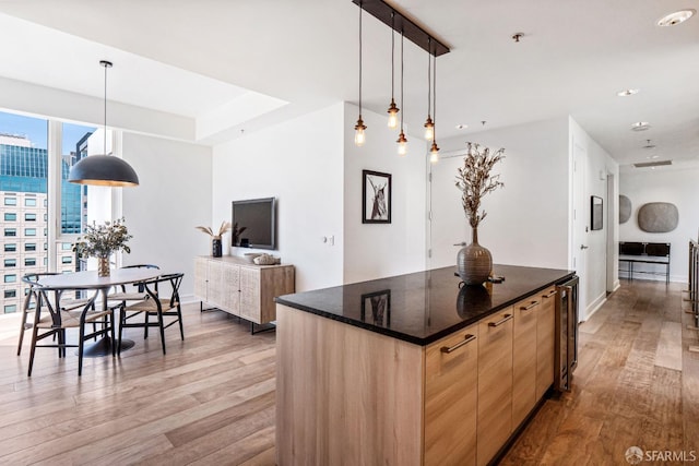 kitchen with light wood-type flooring, dark stone counters, light brown cabinets, and decorative light fixtures