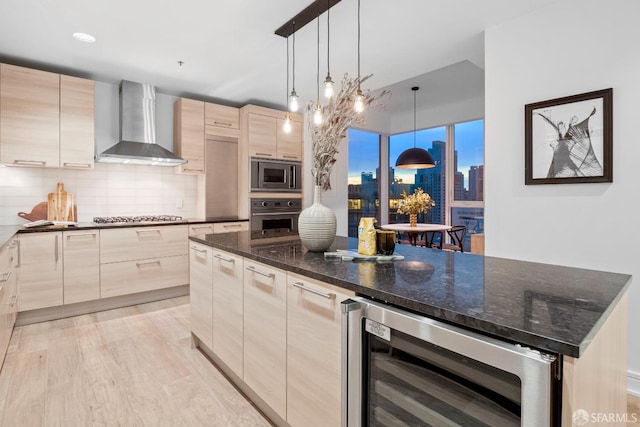 kitchen featuring hanging light fixtures, beverage cooler, wall chimney range hood, stainless steel appliances, and light brown cabinetry