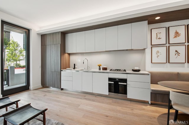 1 Bristol Ct Unit 202, San Francisco, CA 94130 - kitchen featuring oven, white cabinetry, light wood-style floors, a sink, and modern cabinets