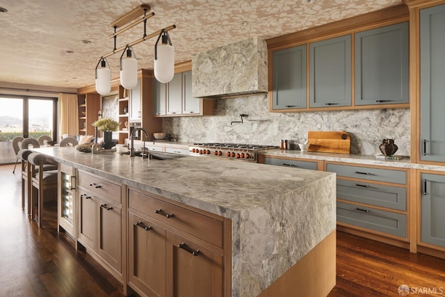 kitchen featuring wall chimney range hood, a sink, light stone countertops, dark wood-type flooring, and backsplash