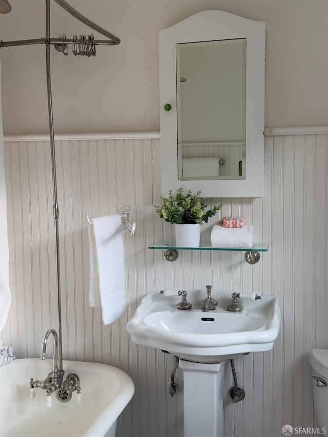 bathroom with a tub to relax in, toilet, and sink