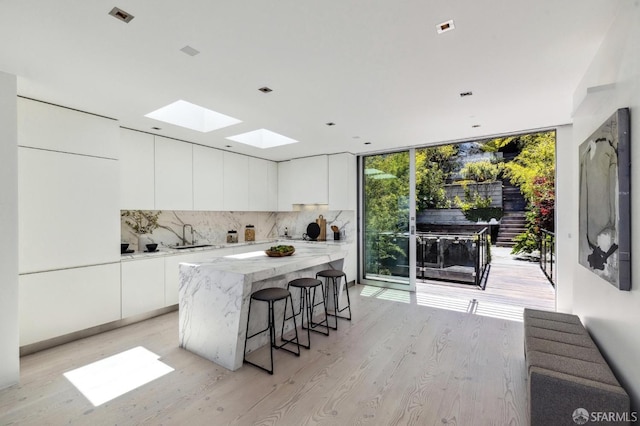 kitchen featuring sink, white cabinetry, a wall of windows, a kitchen island, and decorative backsplash