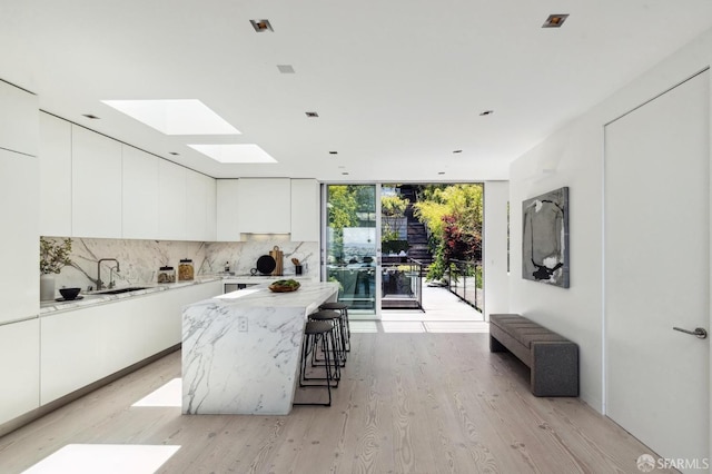 kitchen with tasteful backsplash, white cabinetry, a center island, expansive windows, and light hardwood / wood-style floors