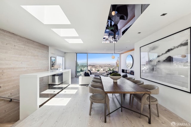 dining room featuring wood walls, light hardwood / wood-style flooring, expansive windows, and a skylight