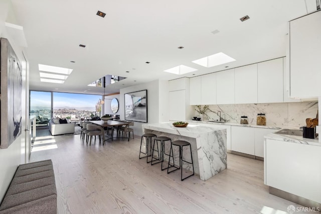 kitchen with decorative backsplash, white cabinets, a kitchen island, sink, and light hardwood / wood-style flooring