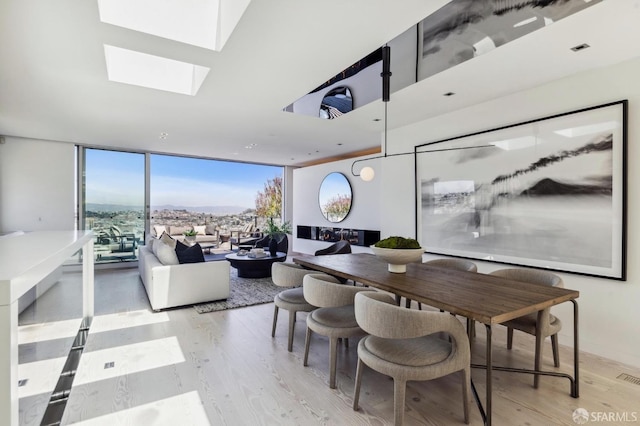 dining room featuring light wood-type flooring, a skylight, and floor to ceiling windows