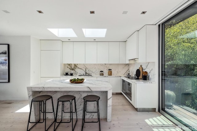 kitchen featuring white cabinets, a center island, backsplash, light wood-type flooring, and a breakfast bar