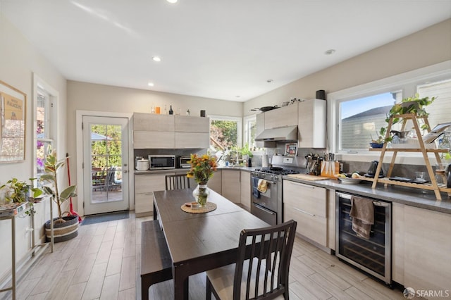 kitchen featuring wood finish floors, stainless steel appliances, modern cabinets, beverage cooler, and under cabinet range hood