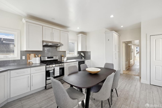 kitchen featuring stainless steel gas stove, under cabinet range hood, light wood finished floors, and backsplash