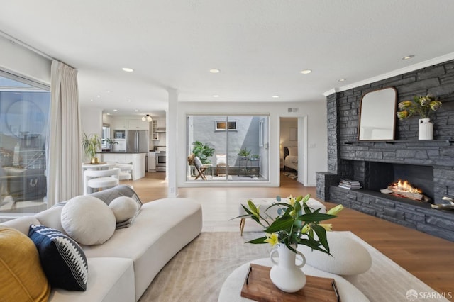 living area featuring light wood-style floors, a stone fireplace, decorative columns, and recessed lighting