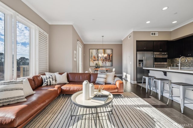 living room with sink, ornamental molding, dark hardwood / wood-style floors, and an inviting chandelier