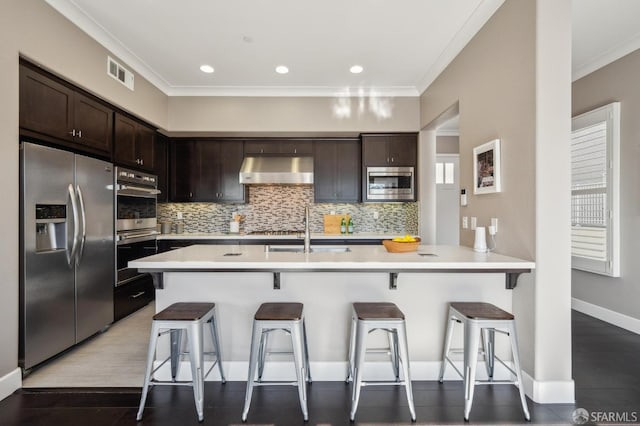 kitchen with a kitchen breakfast bar, ornamental molding, sink, and appliances with stainless steel finishes