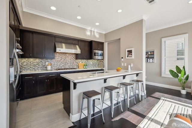 kitchen featuring sink, crown molding, a breakfast bar, a center island with sink, and appliances with stainless steel finishes