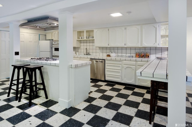 kitchen with stainless steel appliances, tile counters, tasteful backsplash, and white cabinetry