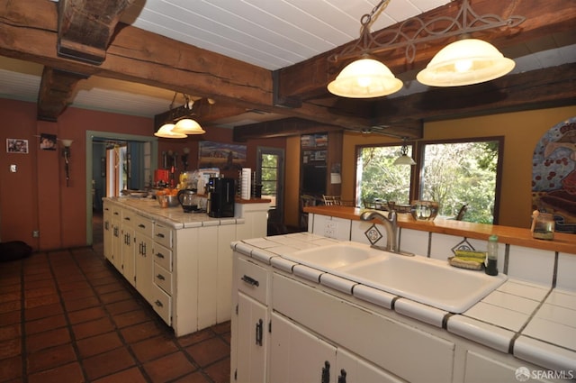 kitchen with tile countertops, a sink, white cabinets, and beamed ceiling