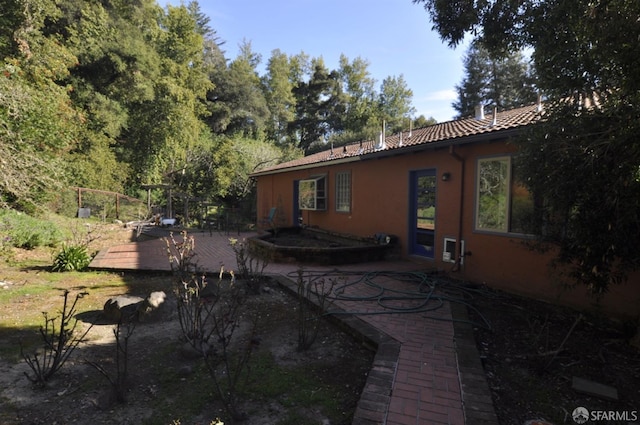 rear view of property featuring a tiled roof, a wooden deck, and stucco siding