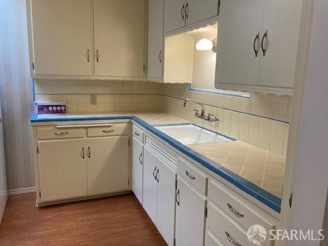 kitchen featuring decorative backsplash, sink, white cabinetry, and dark wood-type flooring