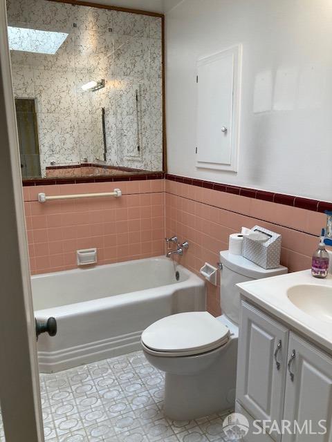 full bathroom featuring tile patterned floors, vanity, a skylight, tile walls, and toilet