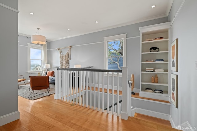 hallway with an upstairs landing, wood finished floors, recessed lighting, and ornamental molding