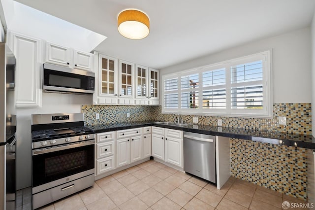 kitchen with a sink, white cabinetry, appliances with stainless steel finishes, dark countertops, and glass insert cabinets