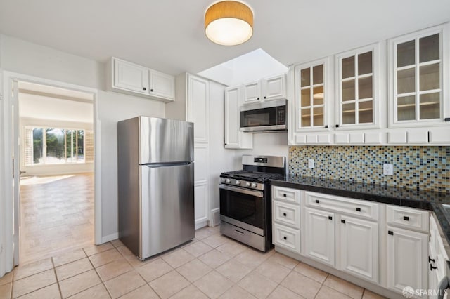 kitchen featuring stainless steel appliances, dark countertops, decorative backsplash, glass insert cabinets, and white cabinetry