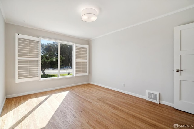 spare room with light wood-style floors, baseboards, visible vents, and crown molding