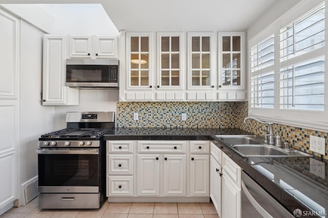 kitchen featuring a sink, white cabinetry, appliances with stainless steel finishes, backsplash, and glass insert cabinets