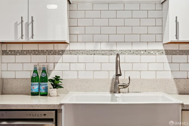 kitchen with tasteful backsplash, white cabinets, dishwasher, light stone countertops, and a sink