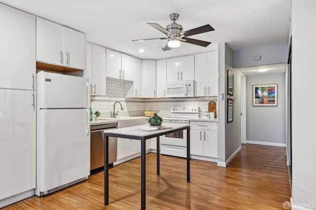 kitchen featuring white appliances, decorative backsplash, white cabinets, light wood-type flooring, and a sink