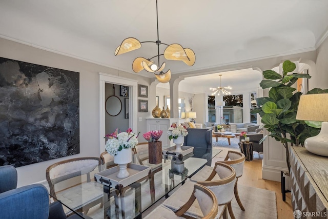 dining room with a chandelier, light wood-type flooring, arched walkways, and ornamental molding