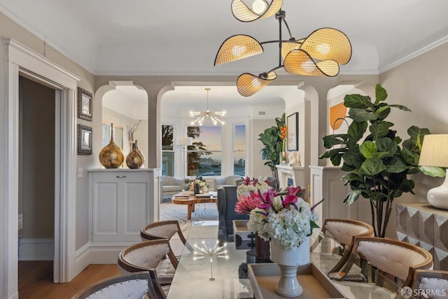 dining area with arched walkways, a chandelier, wood finished floors, baseboards, and crown molding