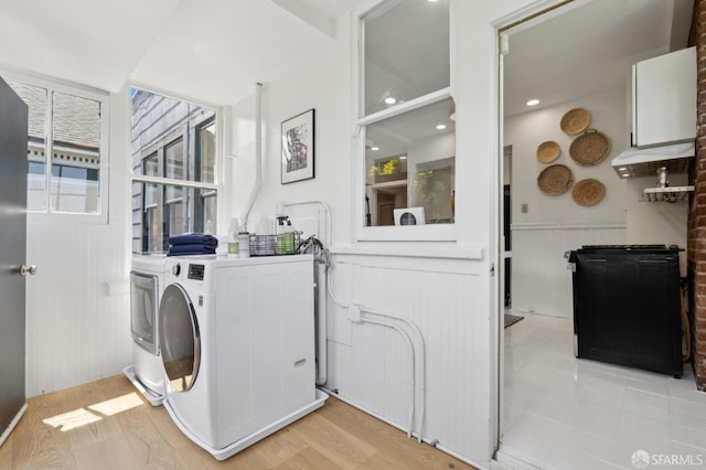 washroom featuring washer and dryer, cabinet space, wainscoting, and a decorative wall