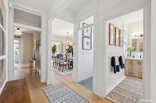 corridor featuring a chandelier, light wood-style flooring, a wainscoted wall, and a decorative wall