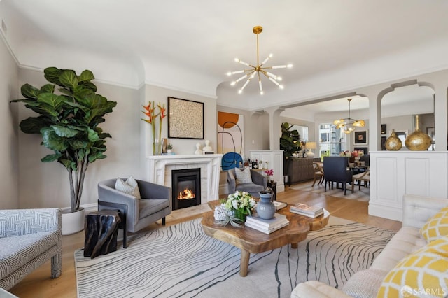 living room with a chandelier, decorative columns, light wood finished floors, a fireplace, and arched walkways