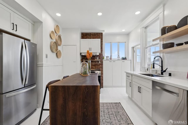 kitchen with appliances with stainless steel finishes, a sink, open shelves, white cabinetry, and wooden counters