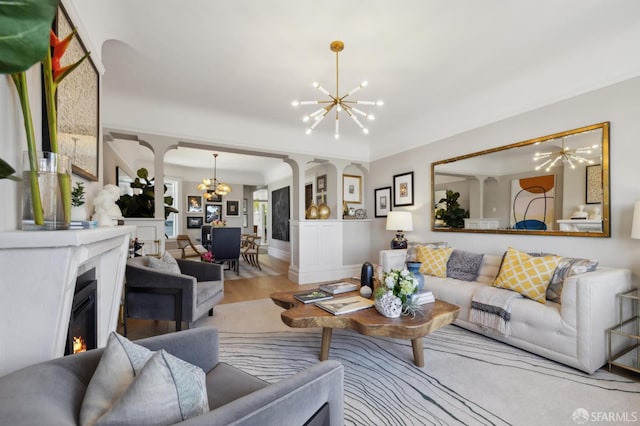 living room featuring a chandelier, arched walkways, wood finished floors, and a lit fireplace