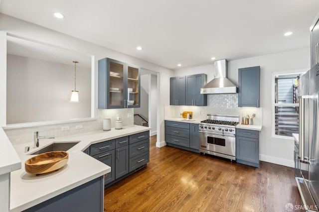 kitchen with hanging light fixtures, high end appliances, dark wood-type flooring, and wall chimney exhaust hood