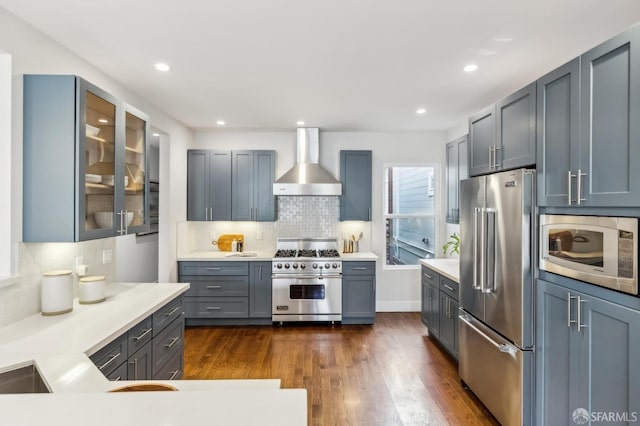 kitchen with dark wood-type flooring, high quality appliances, tasteful backsplash, and wall chimney range hood